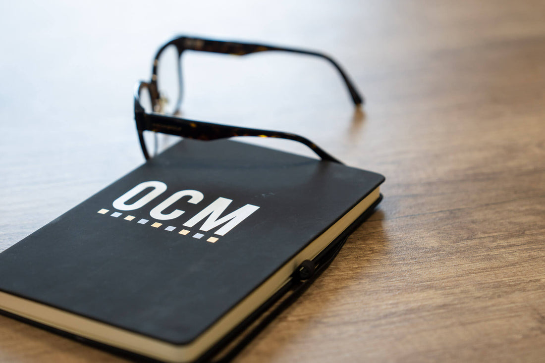 OCM branded notebook on a desk with a pair of glasses